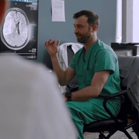 Male physician looking at an x-ray of a brain and explaining it to another person.