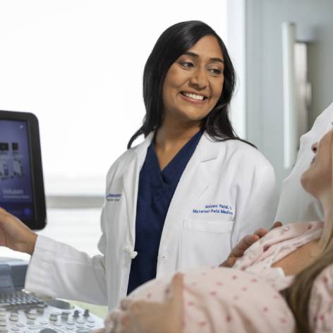 A woman physician pointing at a monitor while looking at a pregnant patient who is laying down and holding her stomach.
