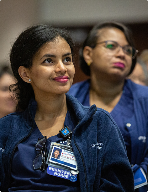 Smiling nurse looking forward in a crowded room surrounded by other seated medical professionals