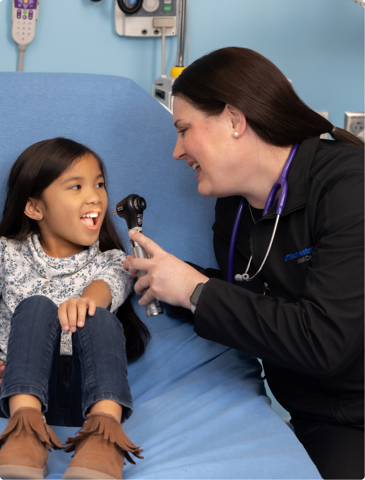 Female pediatric advanced practice provdider employee smiles and examines a young girl in the hospital room