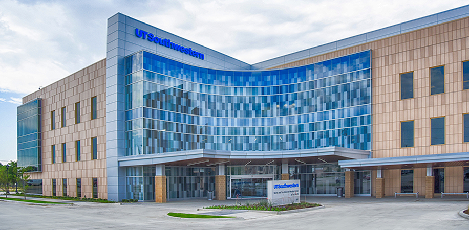 UT Southwestern Fort Worth, a modern building with a curved glass facade and beige paneling, set against a partly cloudy sky.