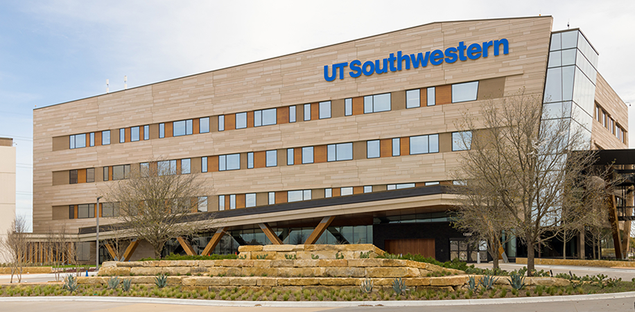 UT Southwestern Frisco, a modern beige building with large windows, wooden accents, and landscaped greenery in front.