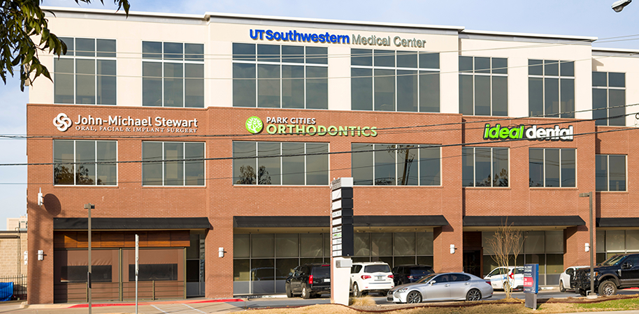 UT Southwestern Medical Center Park Cities, a modern brick and glass building with multiple offices and signage, under a clear sky.