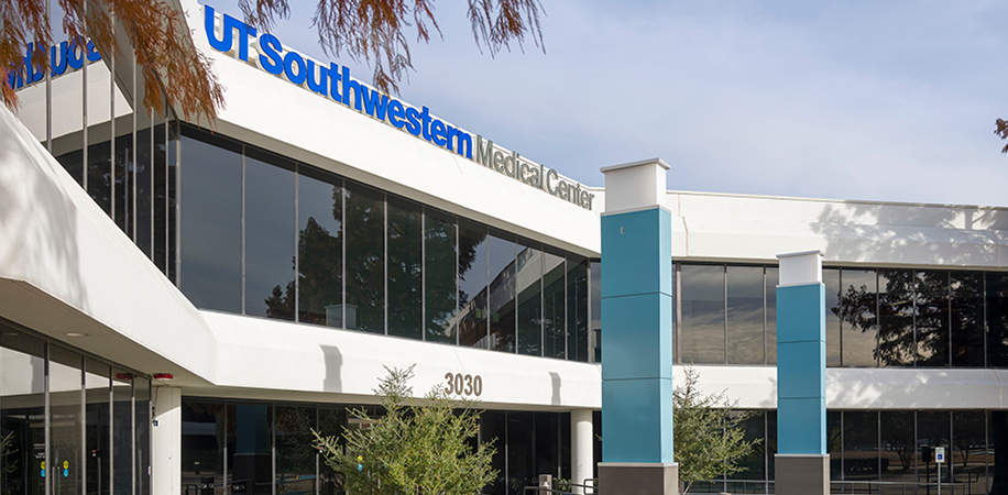 UT Southwestern Medical Center Richardson/Plano, a modern white and glass building with blue accents, surrounded by trees.