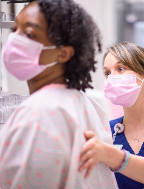 Close-up of a female mammographer helping a gowned patient 